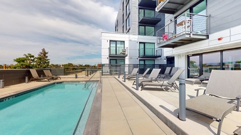 A swimming pool is surrounded by lounge chairs on a patio.