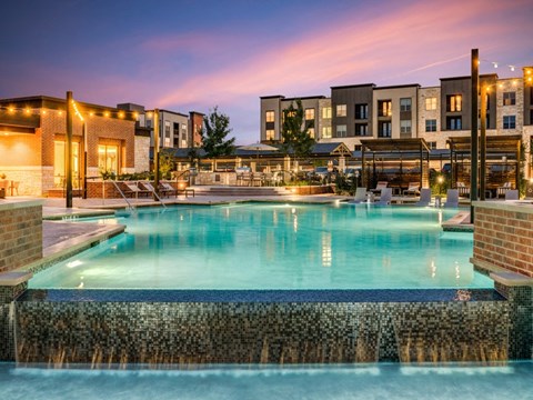 a swimming pool at night with apartments in the background