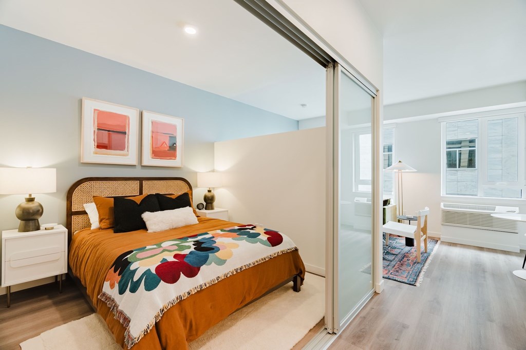 A bedroom with a bed, two lamps, and a painting on the wall.