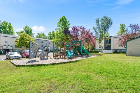 A playground with a green slide and a red car parked in the background.