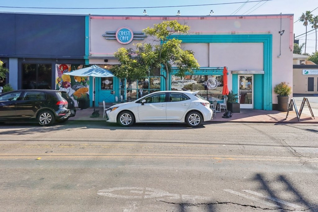 A white car is parked in front of a pink building with a blue door.