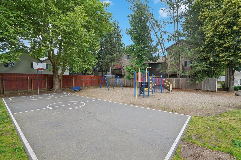 A basketball court is surrounded by a fence and trees.