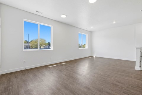 A spacious room with wooden flooring and two windows.