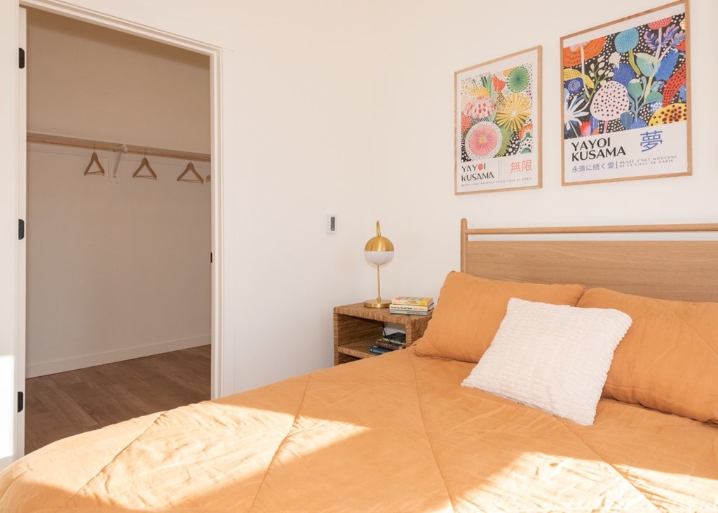 Arts Plaza Gresham Oregon Apartments A bedroom with a bed, a nightstand with a lamp, and two framed pictures on the wall.