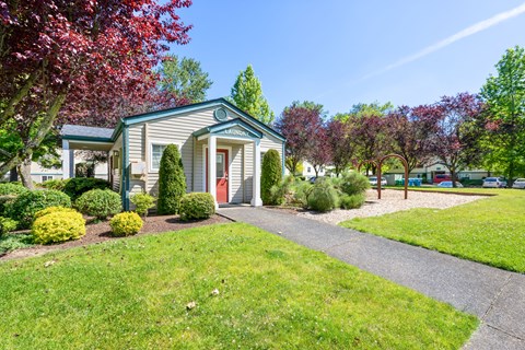 A green house with a red door is surrounded by a well-kept lawn and trees.