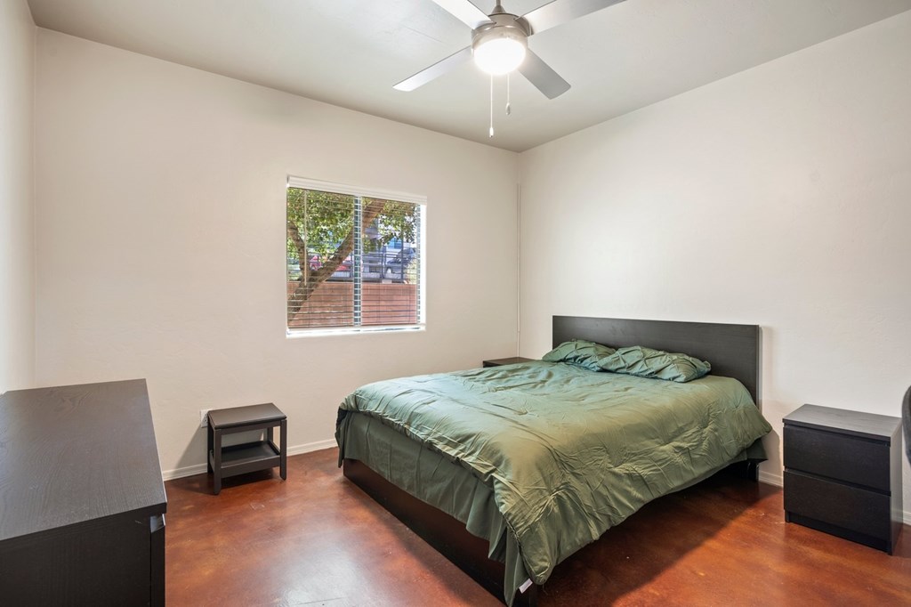 A bedroom with a bed, nightstand, and a window with a view of a backyard.