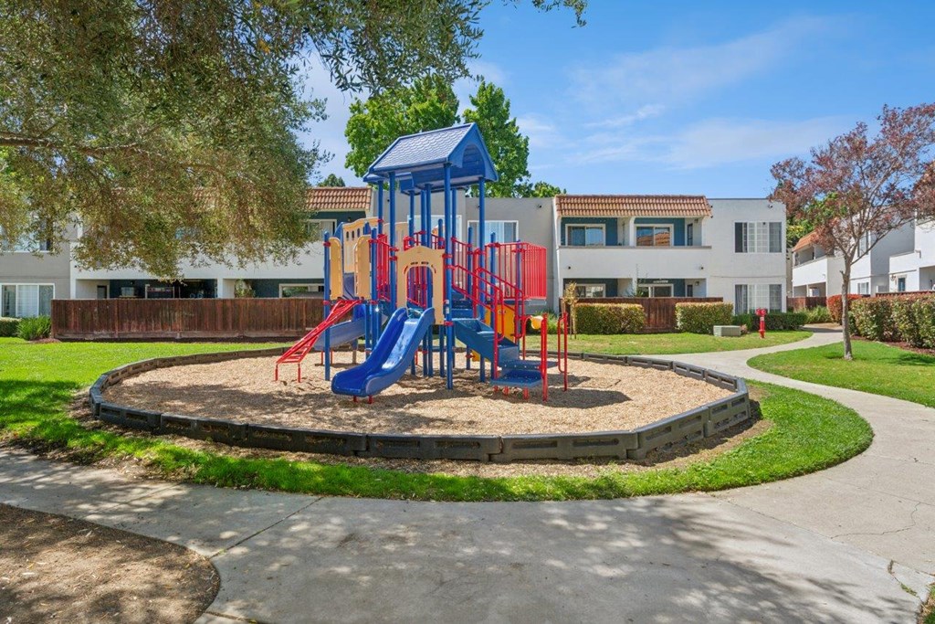 A playground with a blue and red slide in the middle of a grassy area.