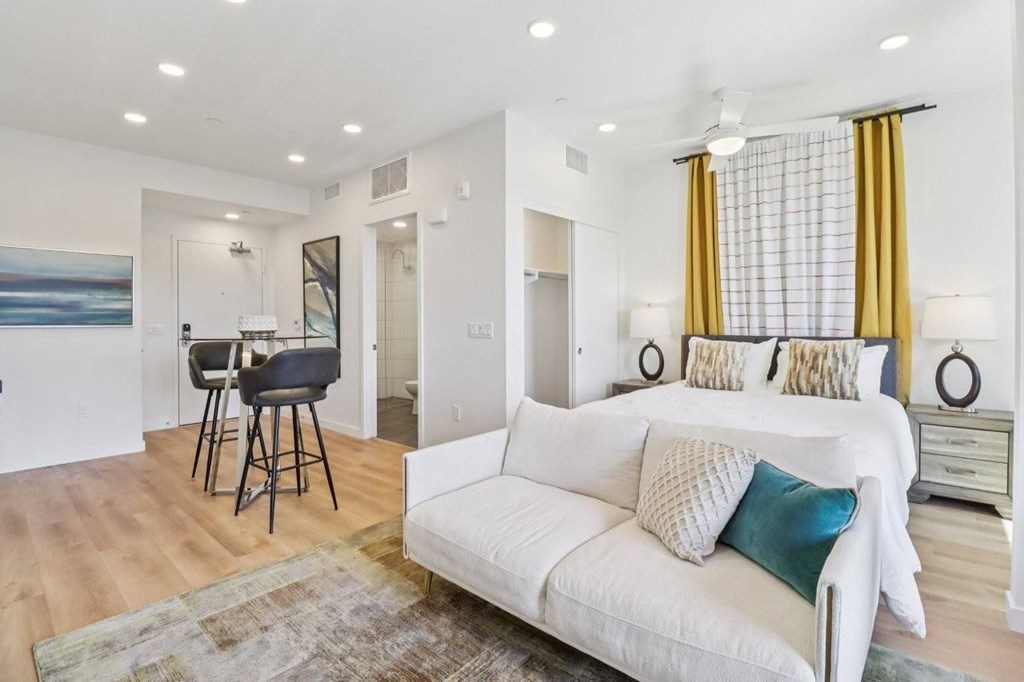 A white couch with blue and white pillows sits in a living room with a bar area and a dining area in the background.