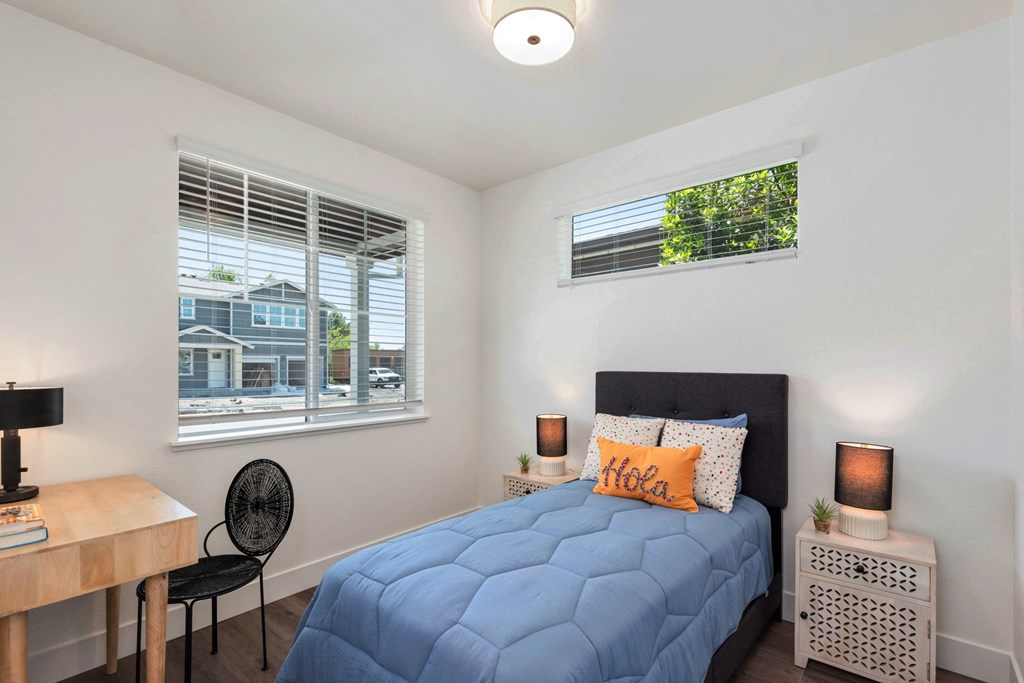 a bedroom with a bed and a desk and two windows
