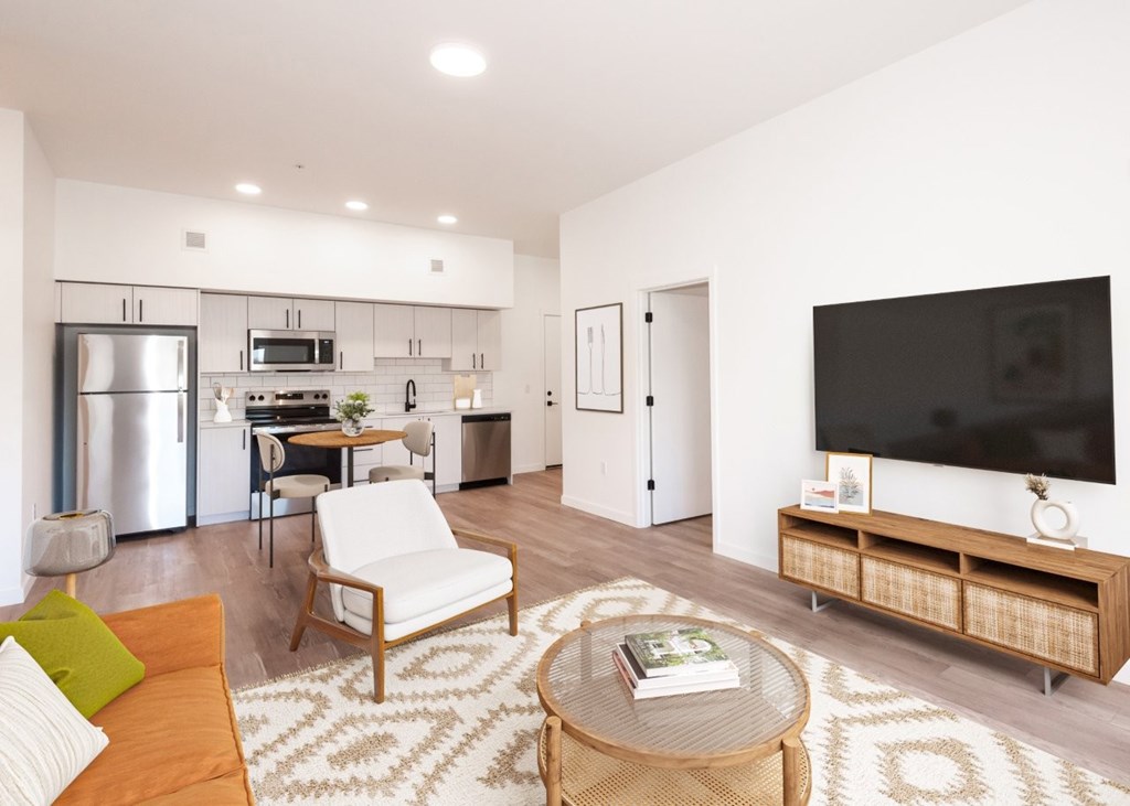 Arts Plaza Gresham Oregon Apartments A modern living room with a refrigerator, a dining table, a sofa, a chair, a coffee table, and a TV.