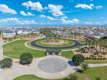 A park with a circular walkway and benches is surrounded by houses.