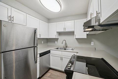 A kitchen with a stainless steel refrigerator and black countertops.