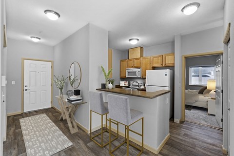 A kitchen with a white fridge and microwave, a wooden table and chairs, and a couch in the background.