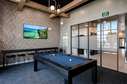 A pool table with a television on the wall and a green exit sign above it.