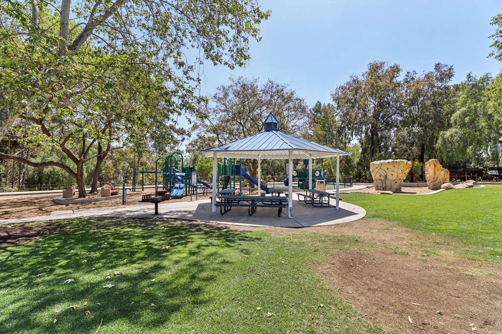 A gazebo sits in the middle of a park with a playground in the background.