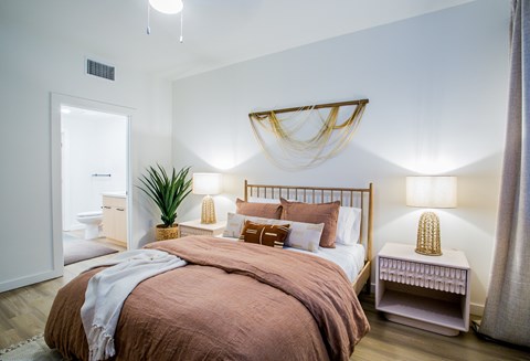 A bedroom with a bed, nightstand, and a plant.