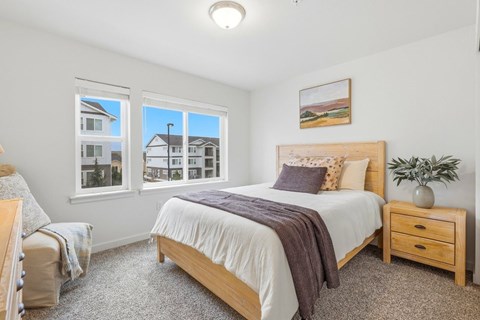 A bedroom with a large bed, a window with a view of a house, and a potted plant on the nightstand.