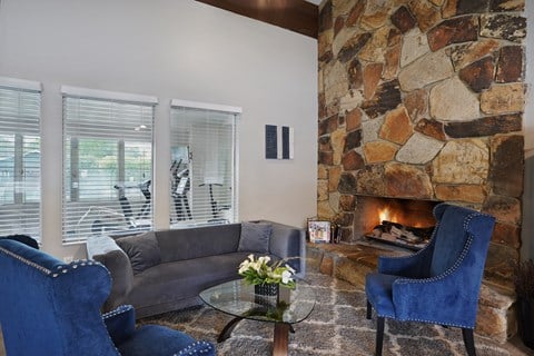 A living room with a stone fireplace and blue chairs.