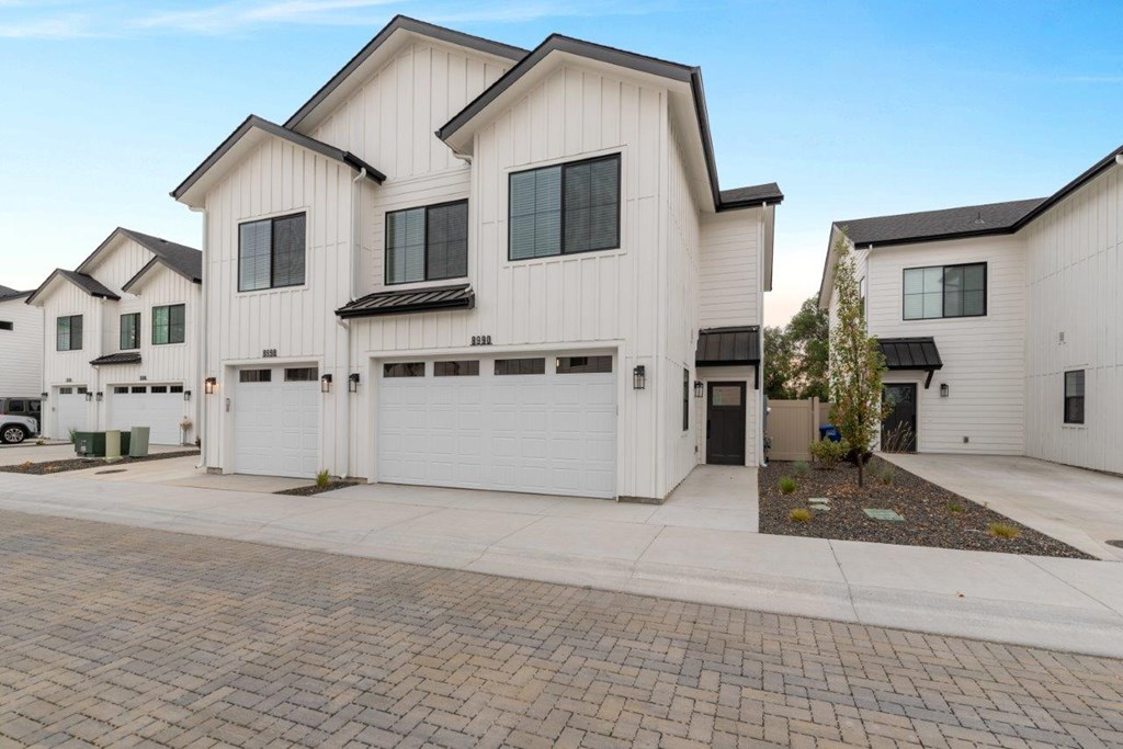 A row of white houses with black roofs and garage doors.