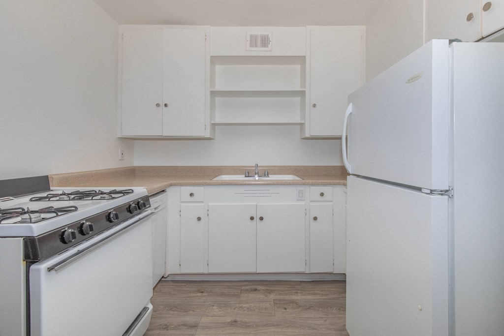 A white kitchen with a stove, sink, and refrigerator.