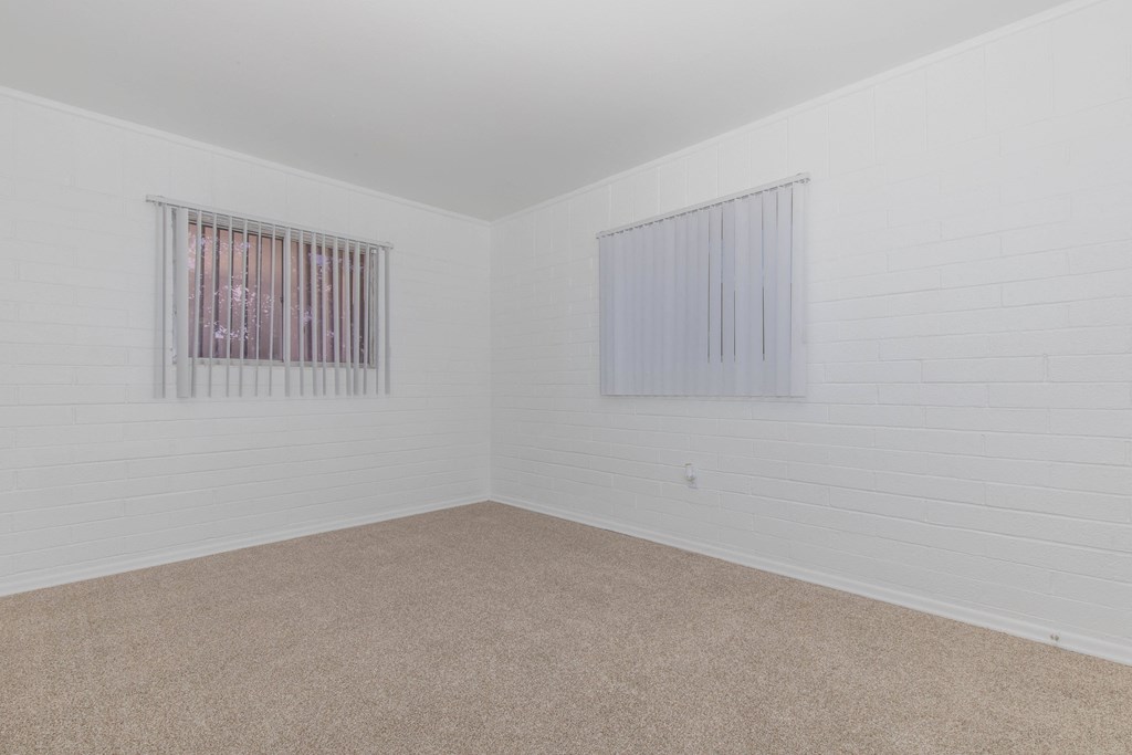A room with a carpeted floor and two windows.