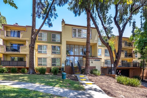 A yellow apartment building with a green trash can in front.