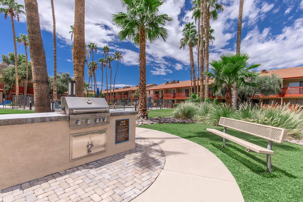 A park with a bench, a grill and palm trees.
