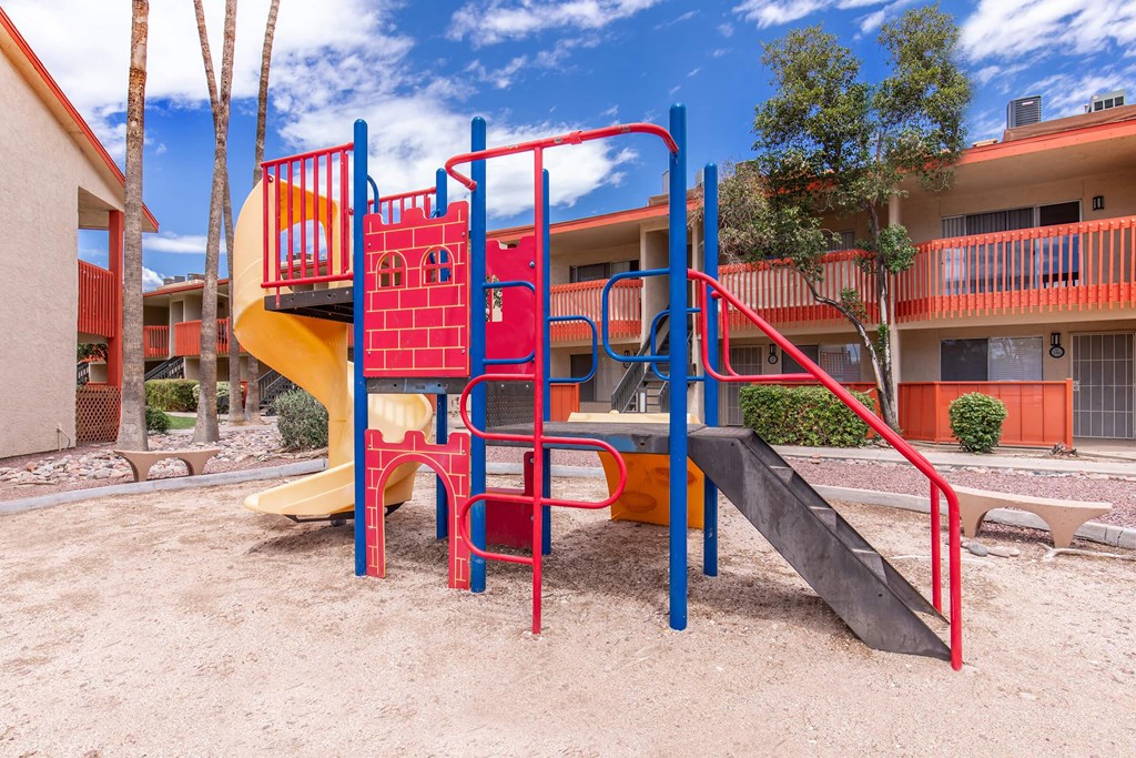 A playground with a red and yellow slide and a red and blue climbing frame.