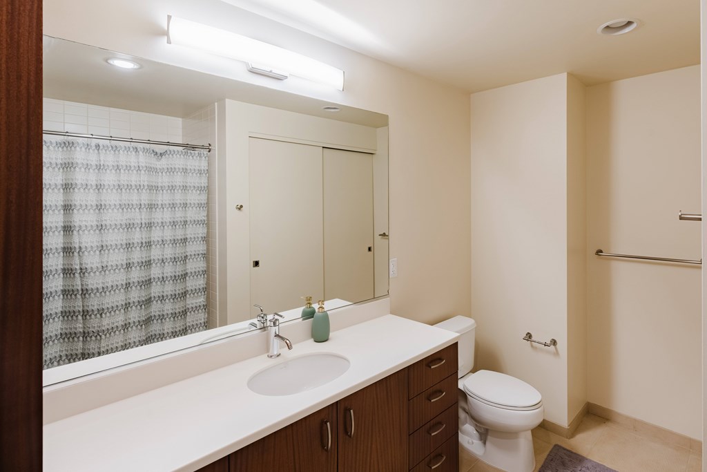 A bathroom with a sink, mirror, toilet, and shower.