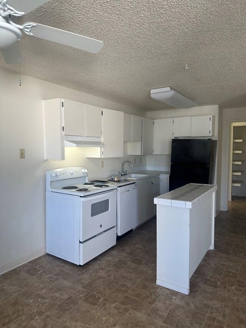 A small white kitchen with a black fridge and a white stove.
