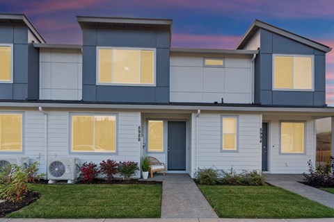A modern two-story house with a front yard and a pathway leading to the entrance.