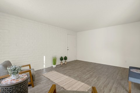 A living room with a grey sofa, a round table with a vase of flowers, a rug, and a small blue ottoman.