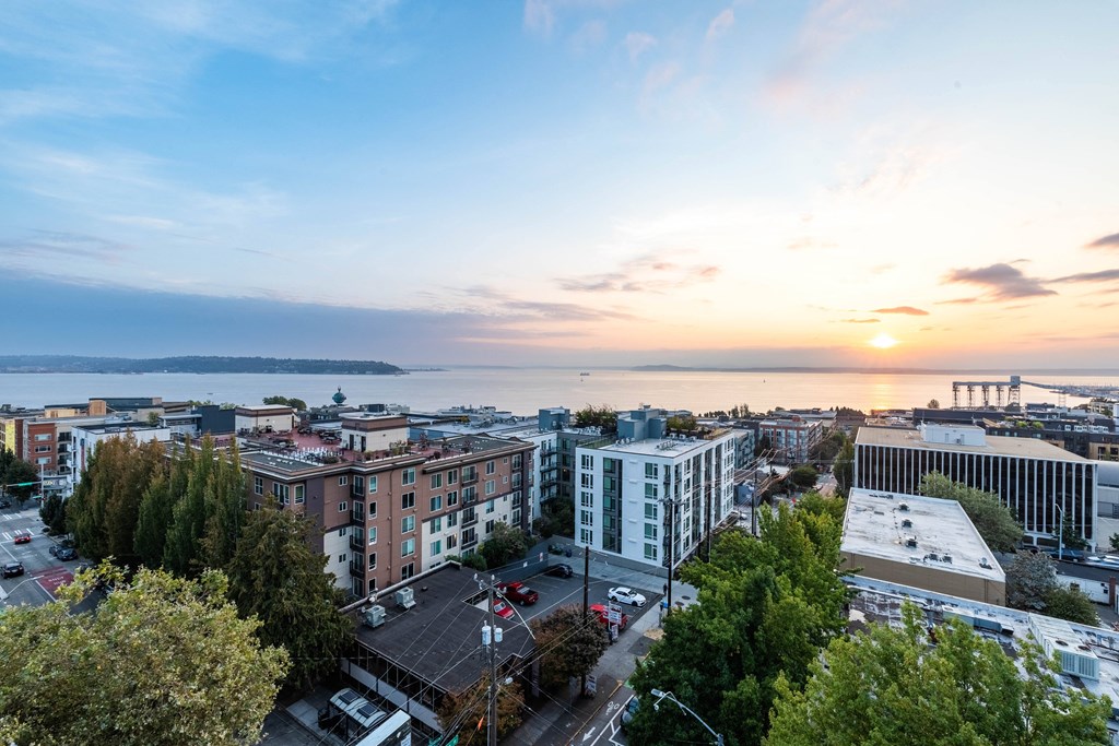 a cityscape with a sunset in the background and a body of water in the distance