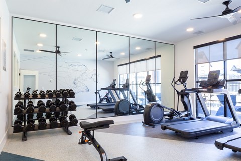 A spacious gym with a variety of equipment including treadmills, stationary bikes, and dumbbells.