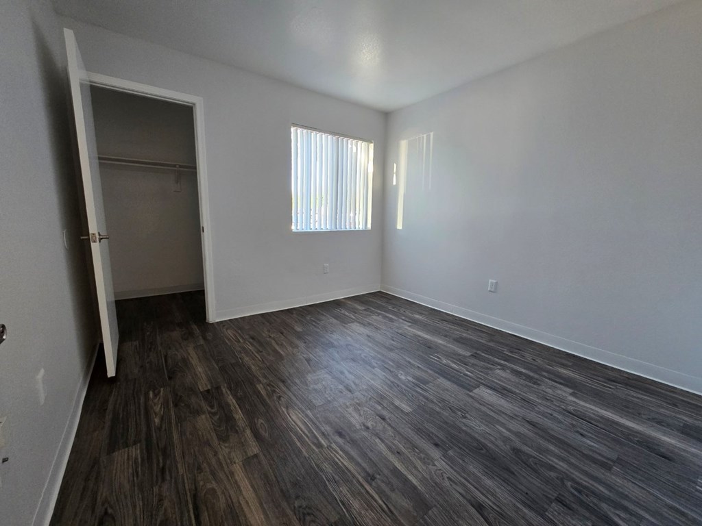 A room with a wooden floor and a window with blinds.