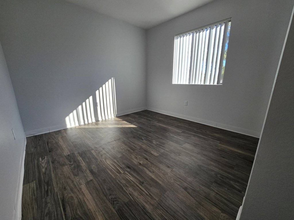 A room with wooden flooring and a window with blinds.