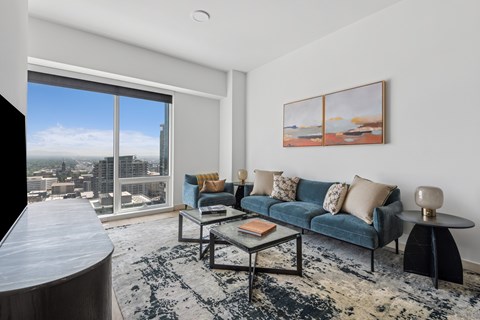 A living room with a blue couch and a large window overlooking a cityscape.