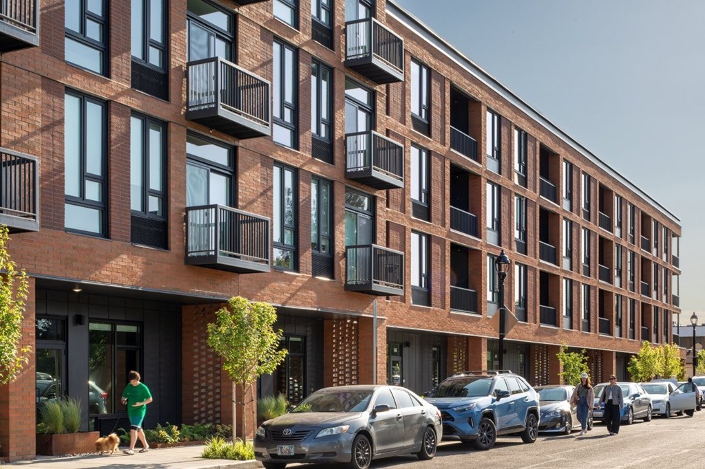 Arts Plaza Gresham Oregon Apartments A red brick building with balconies and cars parked in front.