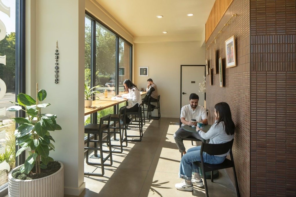 Arts Plaza Gresham Oregon Apartments A man and woman are sitting at a table in a brightly lit room with a potted plant on the left and a brick wall on the right.