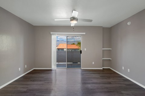 A room with a ceiling fan and a view of a fence and a building outside the window.