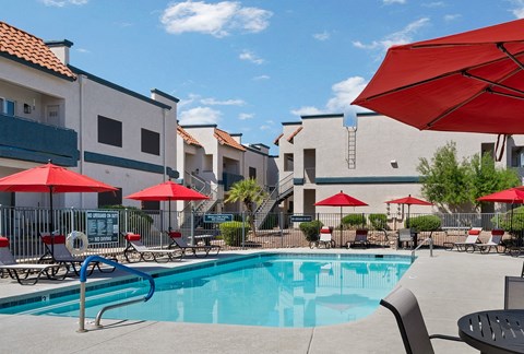 A pool surrounded by red umbrellas and chairs.