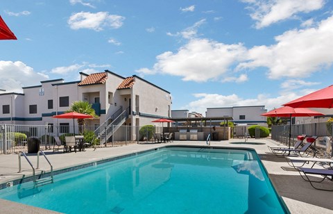 A swimming pool in front of a building with red umbrellas.
