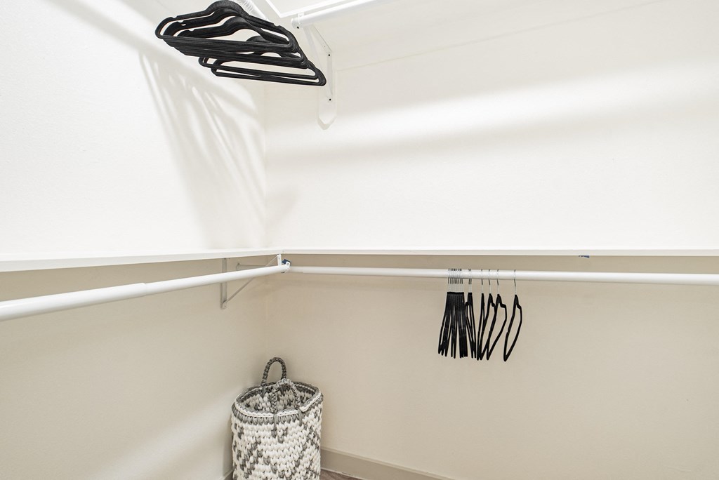 a white closet with a rack of clothes and a basket on the floor