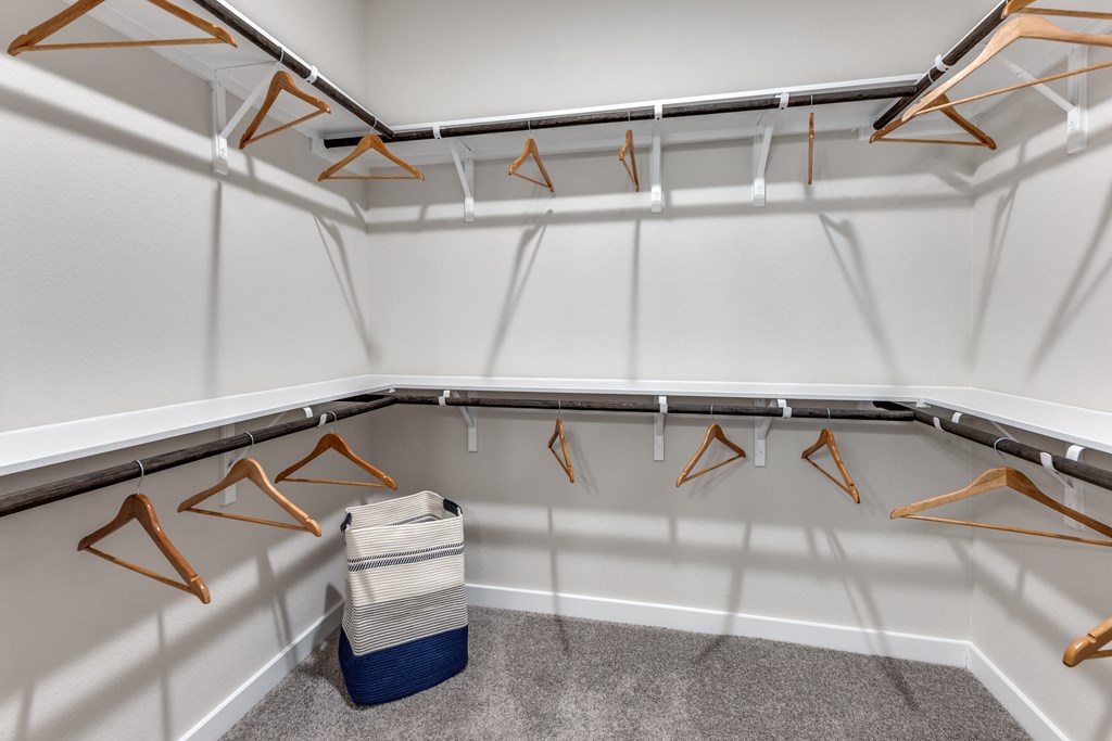 a large closet with clothes hangers and a basket on the floor