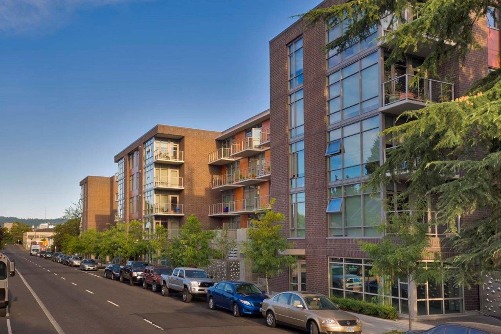 A street view of a residential area with cars parked on the side of the road and modern apartment buildings.