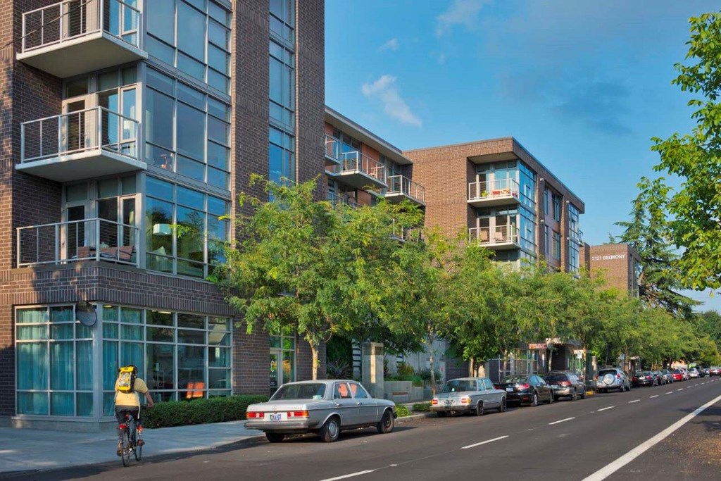 A street view of a residential area with cars parked on the side of the road and a cyclist riding down the street.