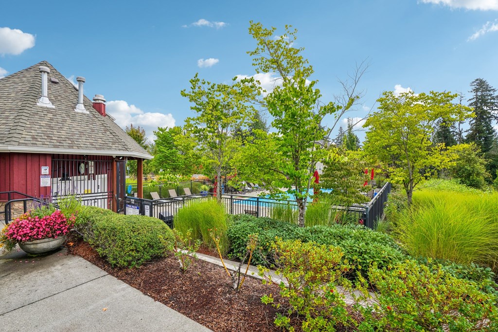 A red building with a grey roof and white chimneys is surrounded by a garden with a variety of plants and trees.