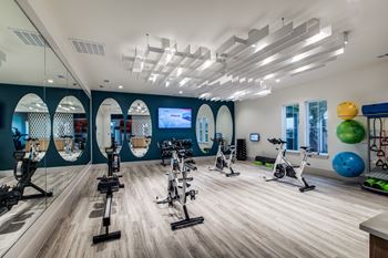 A gym with a variety of exercise equipment including treadmills, stationary bikes, and exercise balls.