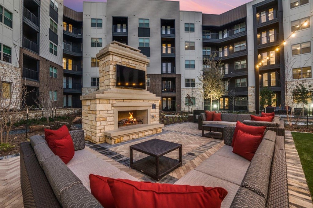 A fireplace is in the middle of a patio with red pillows and a black table.