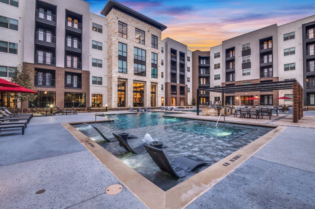 A large outdoor pool surrounded by buildings with a sunset in the background.